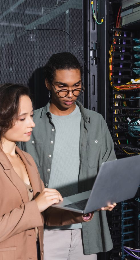 multiethnic technicians working on laptop near server in data center